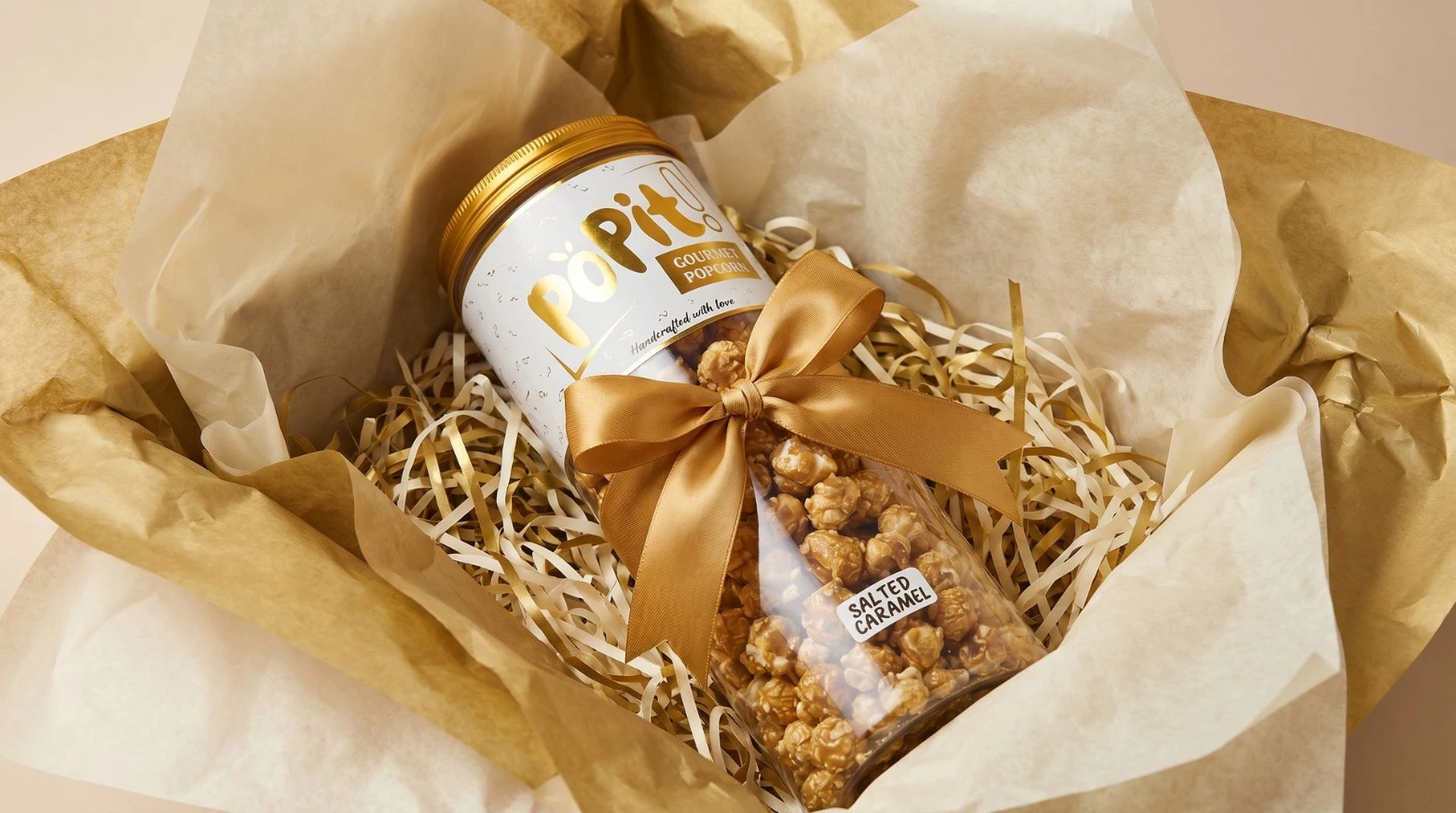 [PACKAGING DETAIL] Close-up of hamper packaging details - tissue paper layers, ribbon tied around a POPIT! jar, shredded paper filler visible. Premium editorial feel.